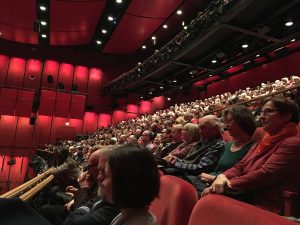 Pełna sala kina z widzami oglądającymi film przy czerwonym oświetleniu