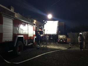 Nocna produkcja filmowa z wozem strażackim i oświetleniem studyjnym