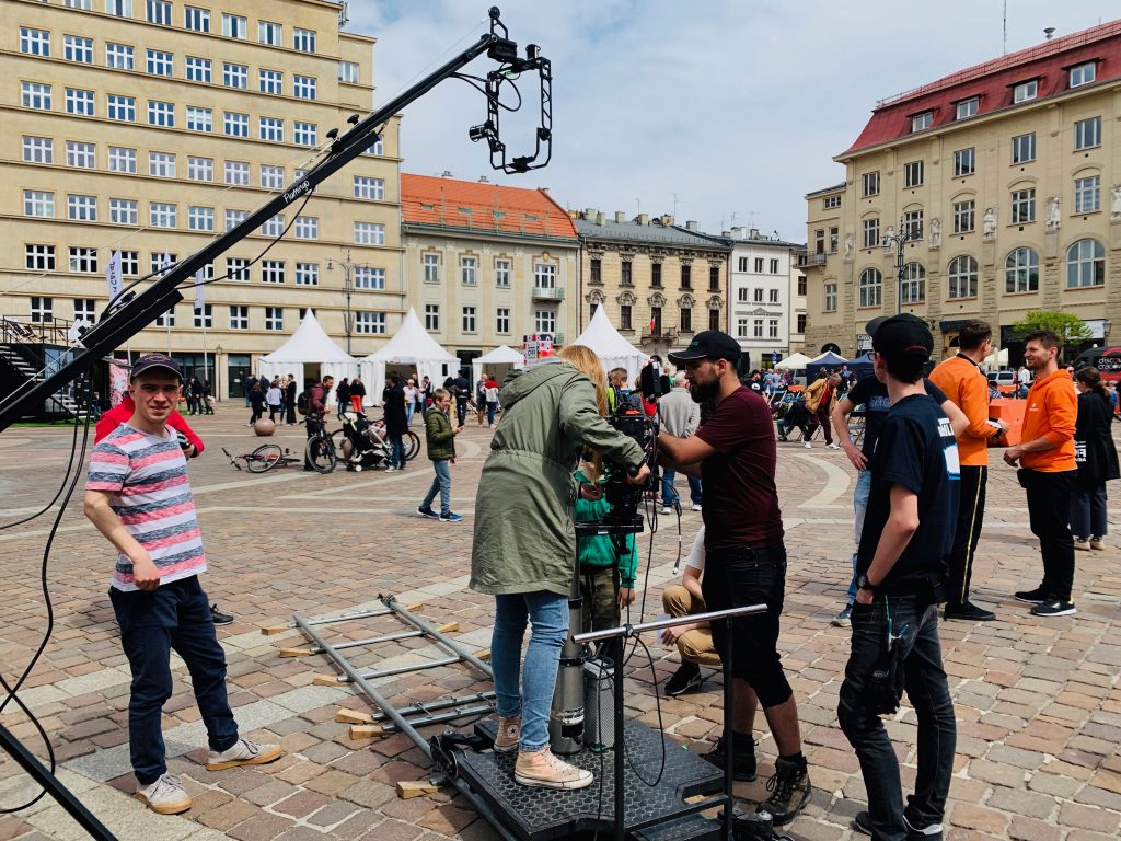 Plac miejski z ekipą filmową podczas zdjęć, kamera na statywie