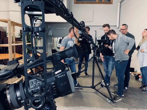 Grupa studentów obserwuje profesjonalny sprzęt filmowy i kamerę na statywie