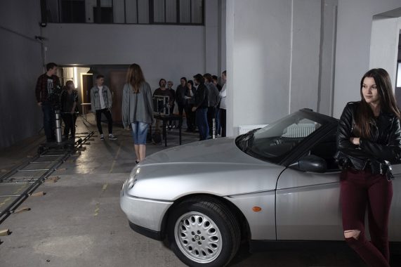 Kobieta przy srebrnym samochodzie, zespół produkcji filmowej w tle