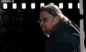 Mężczyzna w okularach i ciemnej kurtce patrzy w bок