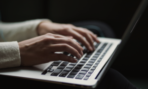 Ręce osoby piszącej na klawiaturze laptopa w ciemnym otoczeniu