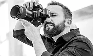 Brodaty mężczyzna z kamerą filmową przy oku, czarno-białe zdjęcie