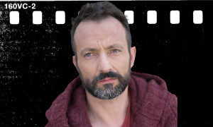 Portret mężczyzny z brodą w bordowej koszuli na ciemnym tle