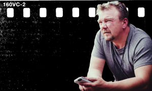 Mężczyzna w szarej koszulce siedzi i gestykuluje podczas wykładu o filmie