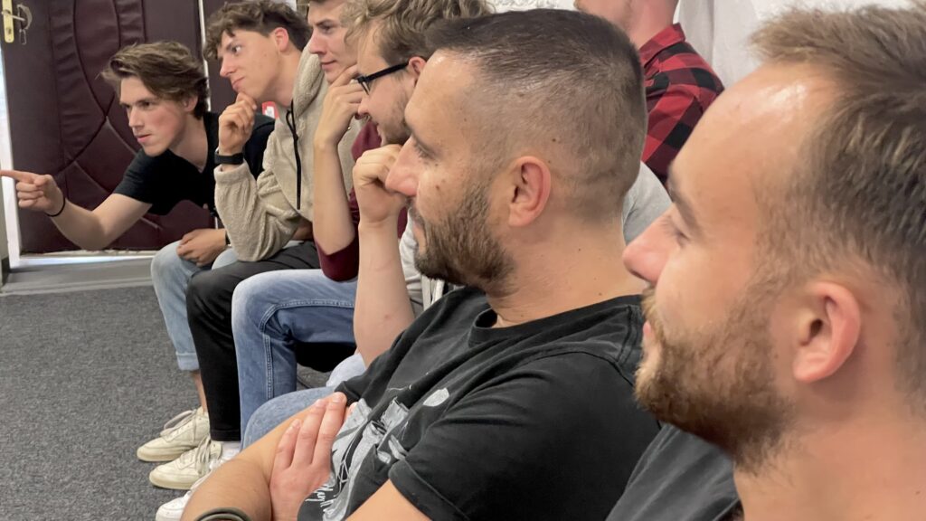 Grupa mężczyzn siedzi razem na warsztatach szkoły filmowej AMA