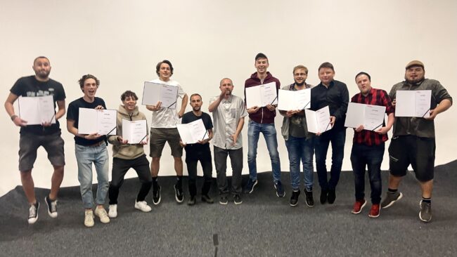 Grupa absolwentów AMA Film Academy trzymająca dyplomy ukończenia szkoły filmowej