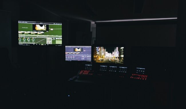 Stanowisko pracy postprodukcji z wieloma monitorami i sprzętem edycyjnym w ciemnym studiu