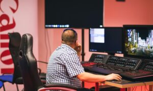 Mężczyzna pracuje przy stanowisku postprodukcji z wieloma monitorami i sprzętem audio