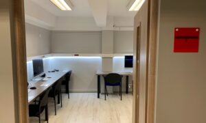 Nowoczesna sala komputerowa z biurkami, monitorami i czarnymi krzesłami