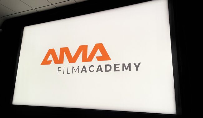 Logo AMA Film Academy wyświetlane na białym ekranie projekcyjnym w ciemnej sali
