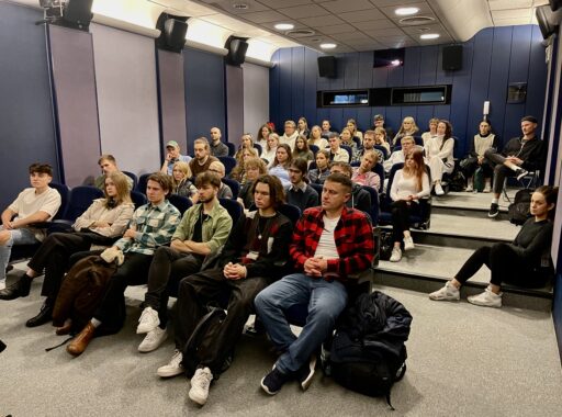 Duża grupa studentów sfilmów siedzi i stoi w sali szkoleniowej AMA