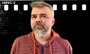 Mężczyzna w czerwonej koszuli w paski patrzy w kamerę na tle filmu