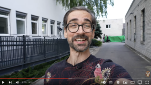 Mężczyzna w okularach uśmiecha się do kamery na terenie szkoły filmowej