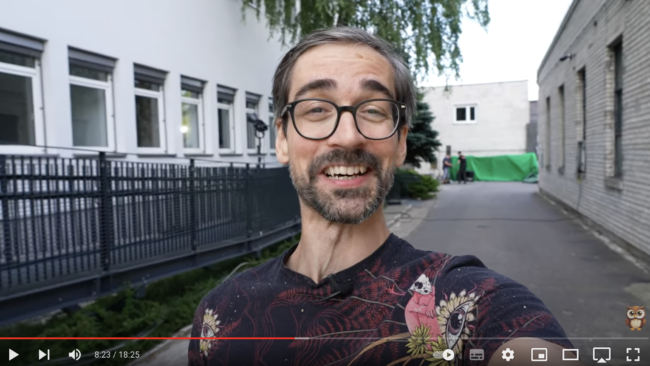 Mężczyzna w okularach uśmiecha się do kamery na terenie szkoły filmowej