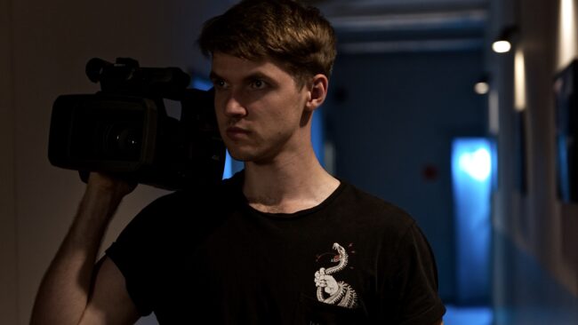 Mężczyzna z kamerą wideo na ramieniu w ciemnym studiu filmowym